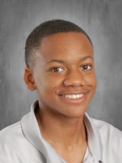 Smiling Black teen in a gray shirt poses for a school portrait against a gray background.
