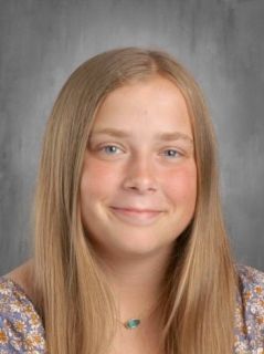 Blonde girl with a slight smile and turquoise necklace, posing for a portrait.