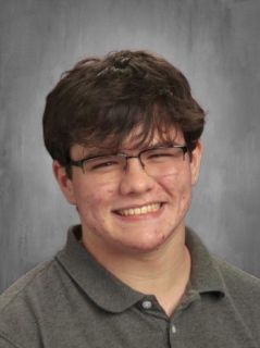 Teenage boy with glasses, smiling, wearing a gray polo shirt, studio portrait.
