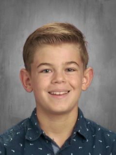 Smiling boy with fair skin and short brown hair in a blue shirt.