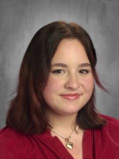 Young woman with auburn hair, wearing a red top and pearl necklace, smiling.