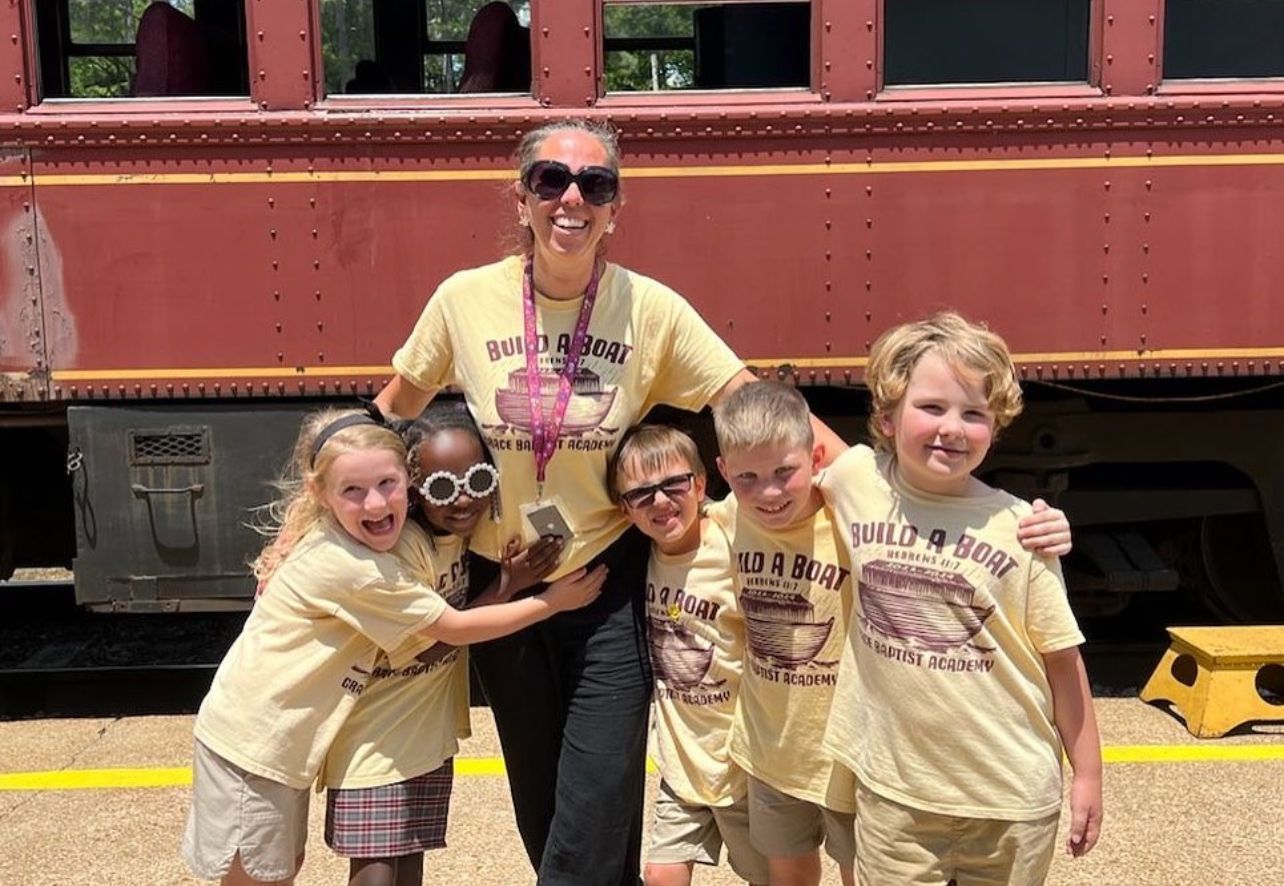 Woman and five children wearing matching t-shirts, smiling in front of a maroon train car.