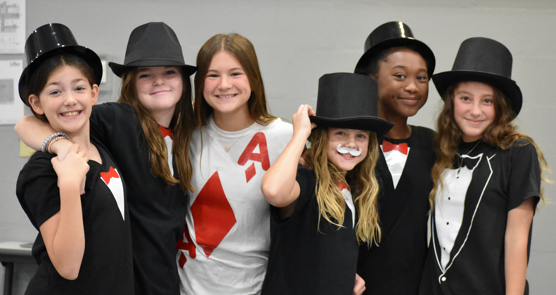 Group of kids dressed as magicians, wearing top hats and playing card suits. They are smiling.