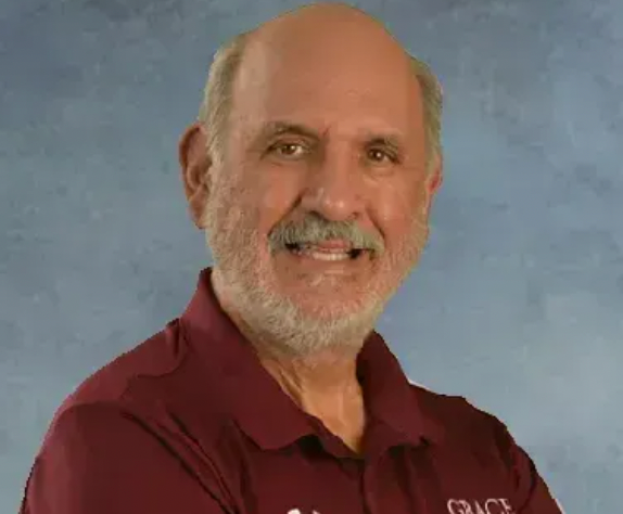 Smiling older man with a gray beard and mustache, wearing a maroon polo shirt.