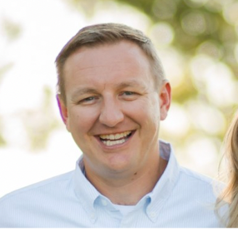 Man smiling, light blue shirt, outdoors, natural light.