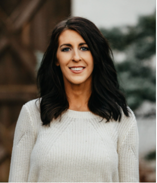 Woman with dark hair, smiling, wearing a white sweater, outdoors.