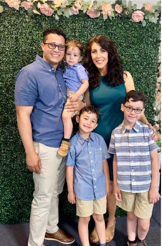 Family of five poses in front of a green wall with flowers.
