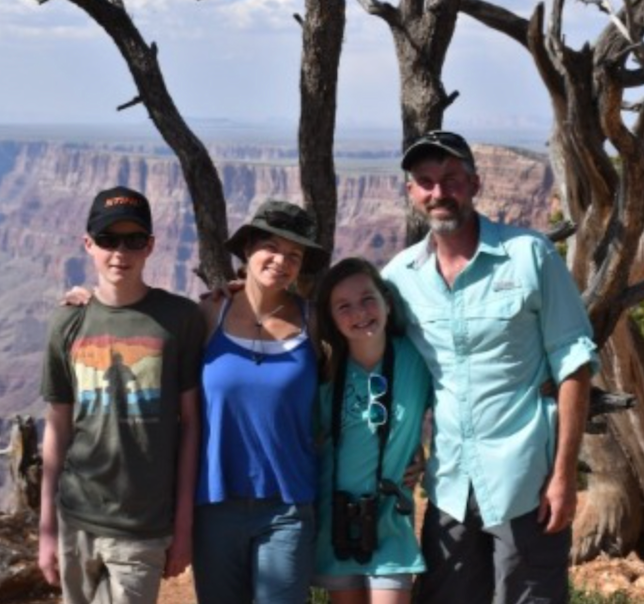 Family poses in front of the Grand Canyon, with a tree in the foreground.