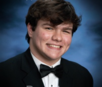 Young man in a tuxedo smiles broadly against a blue background.
