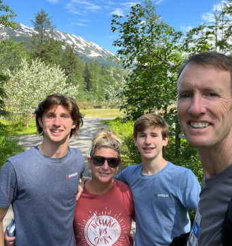 Family smiling for a selfie outdoors with mountains in the background.