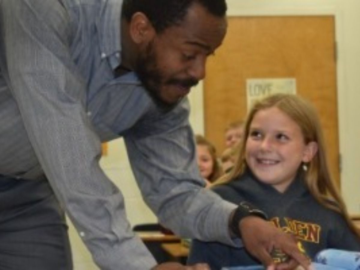 Teacher helping a smiling girl at her desk in a classroom.