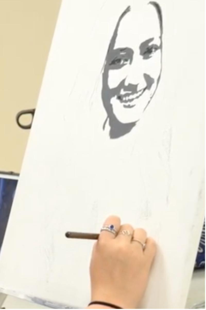 Hand sketching portrait onto canvas, a light-skinned person with dark hair smiling.