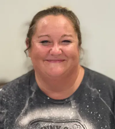 Woman with light skin smiling, wearing a grey top with a white splotchy design.