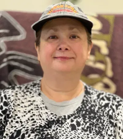 Woman wearing a cap, smiling, in front of a brown patterned background.
