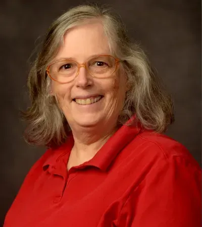 Woman with glasses and gray hair wearing a red shirt smiles at the camera.