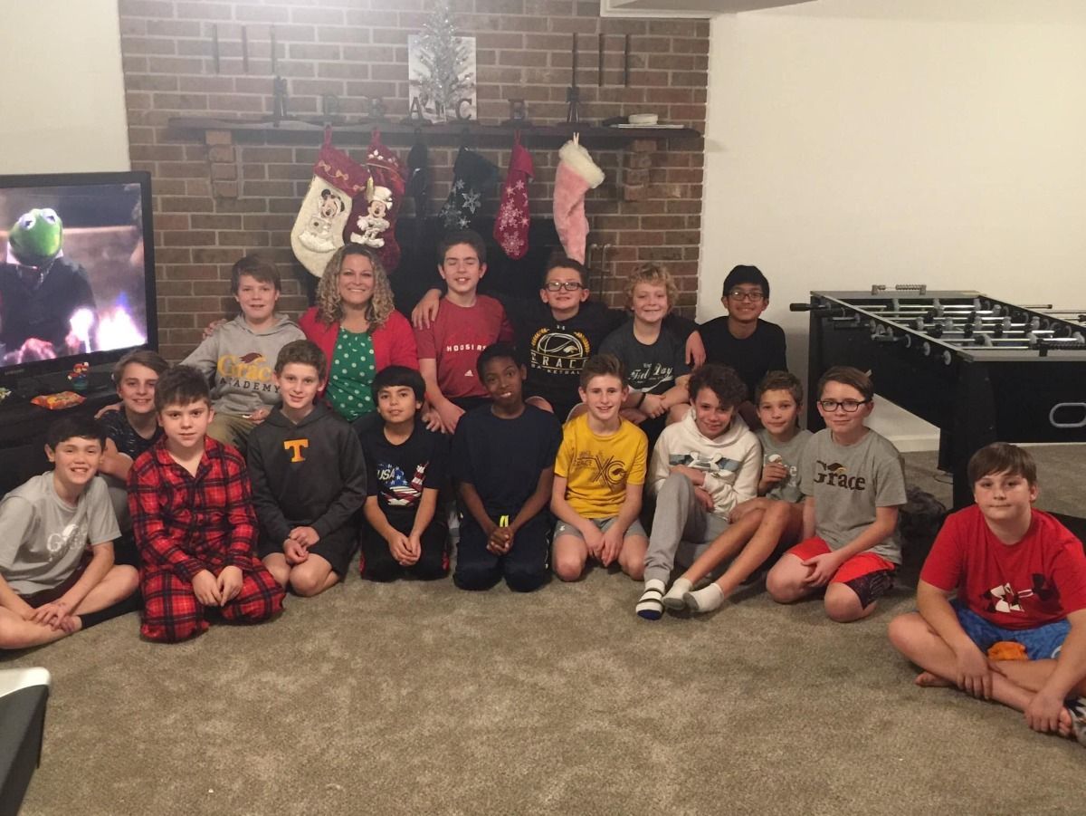 Group of kids posing in front of a fireplace with Christmas stockings. Some are smiling, indoors.