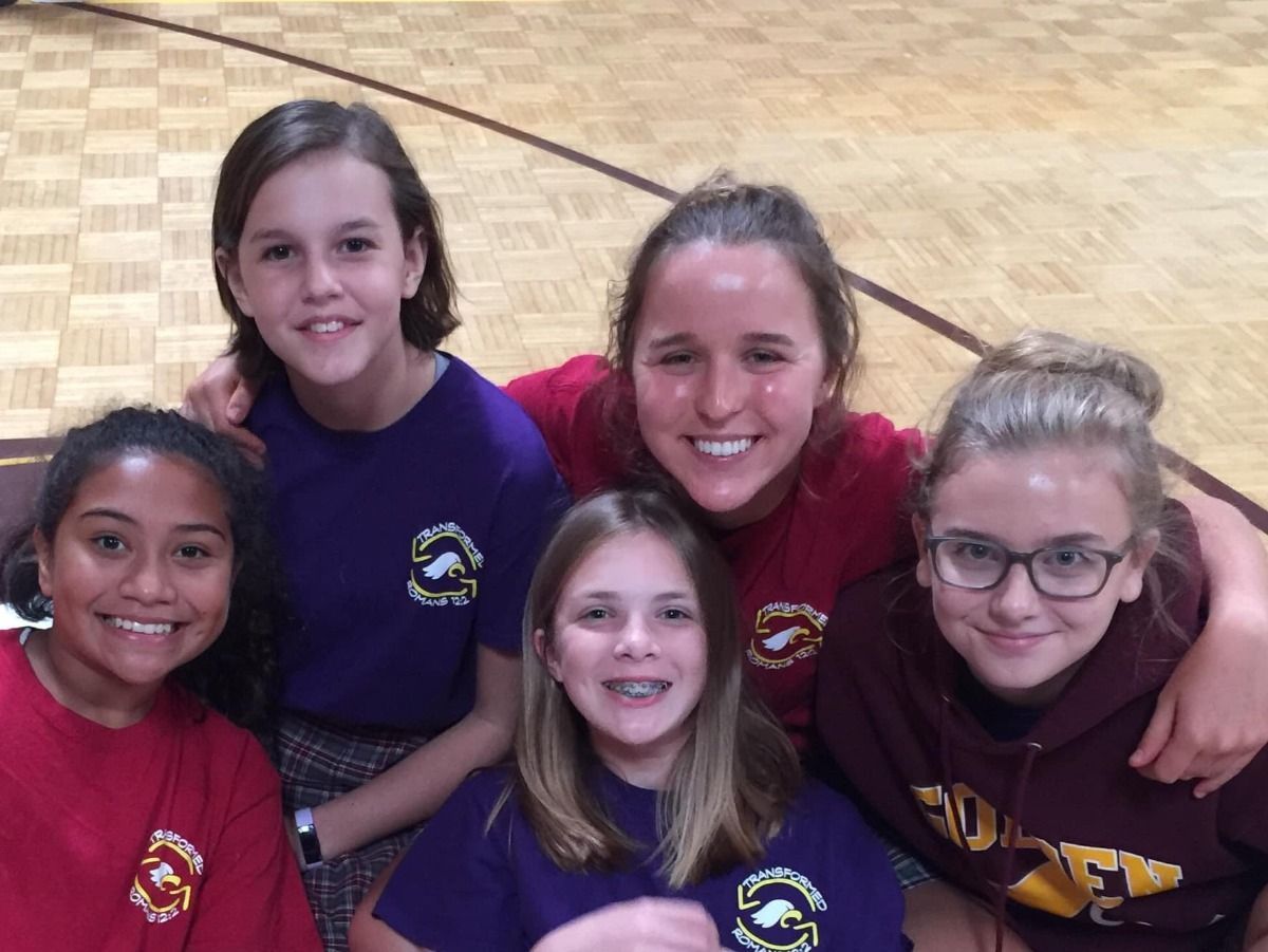 Five smiling girls in maroon and purple shirts, arms around each other.