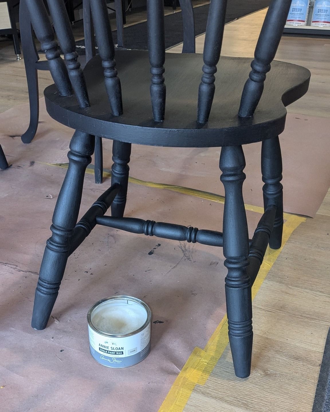 A black wooden chair is sitting next to a small can of paint.