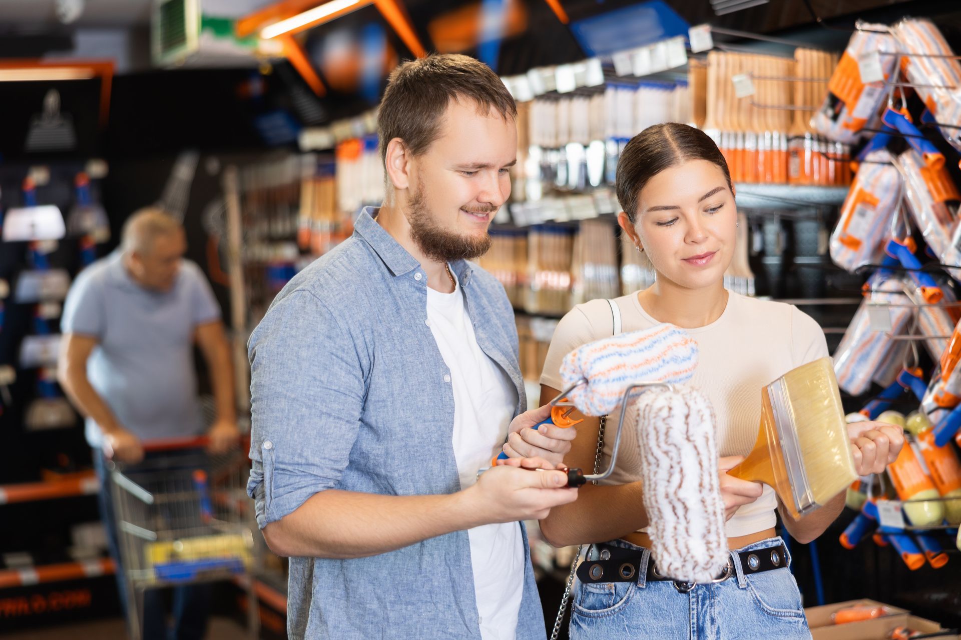 A couple choosing a paintbrush and paint roller together at a paint supply store.