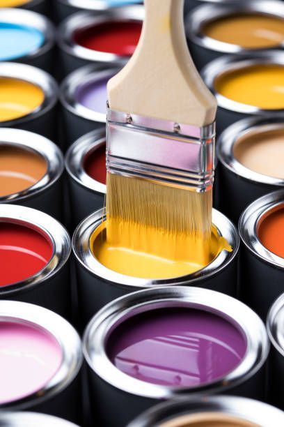 A brush is dipping into a can of yellow paint