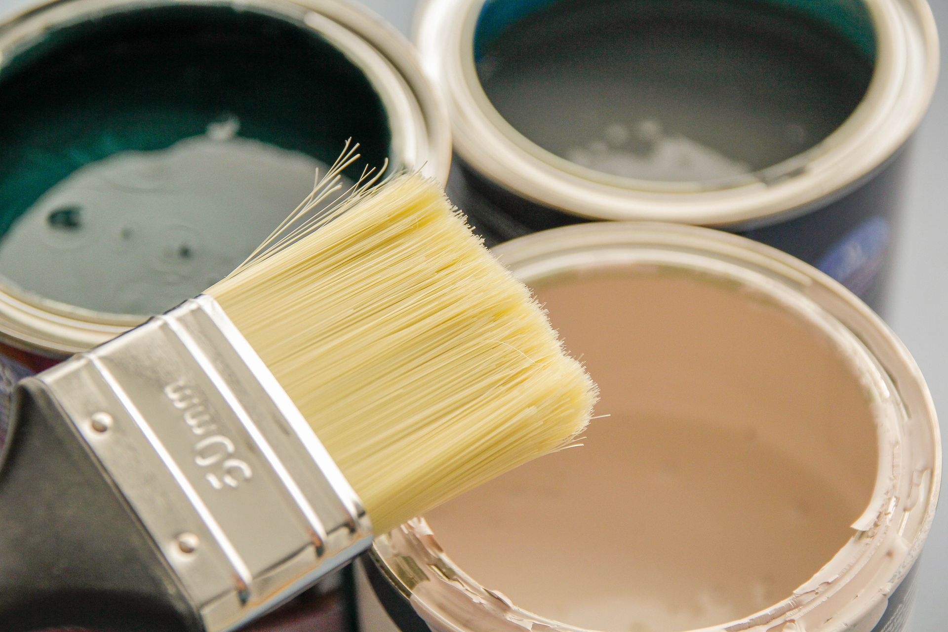 Three open paint cans with dark green, blue, and beige colors; brush above. Three open paint cans with dark green, blue, and beige colors; brush above.