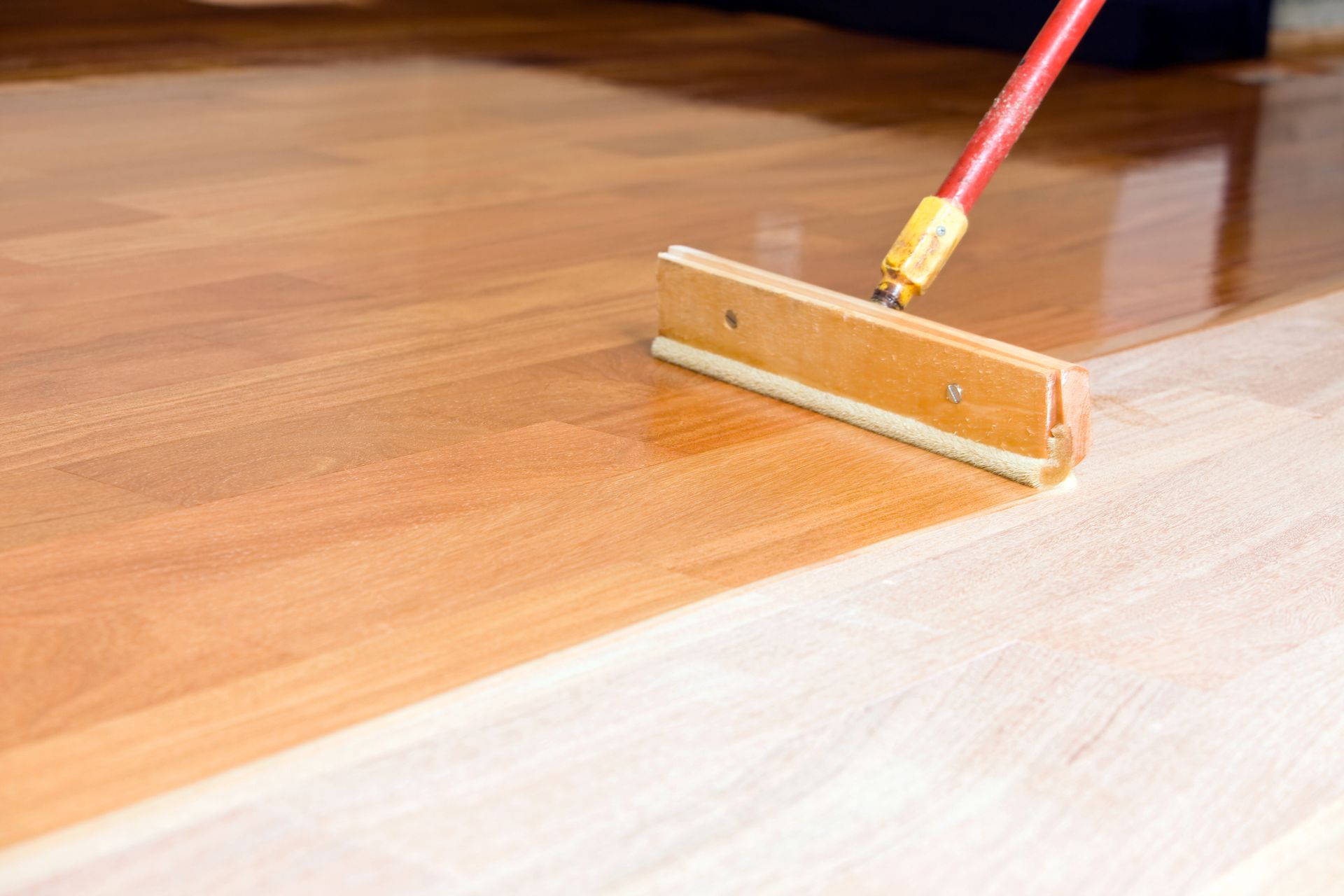 A person is painting a wooden floor with a broom.