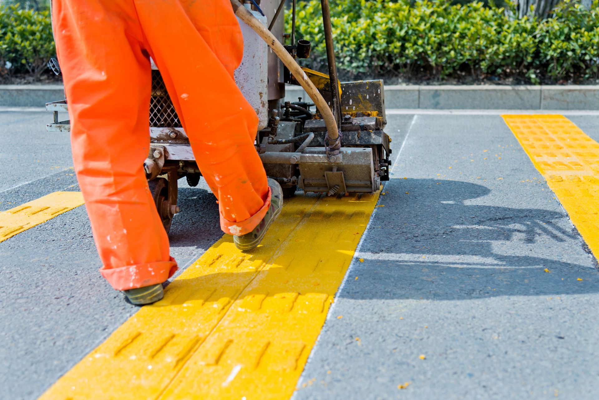 A man in orange pants is painting a yellow line on the road.