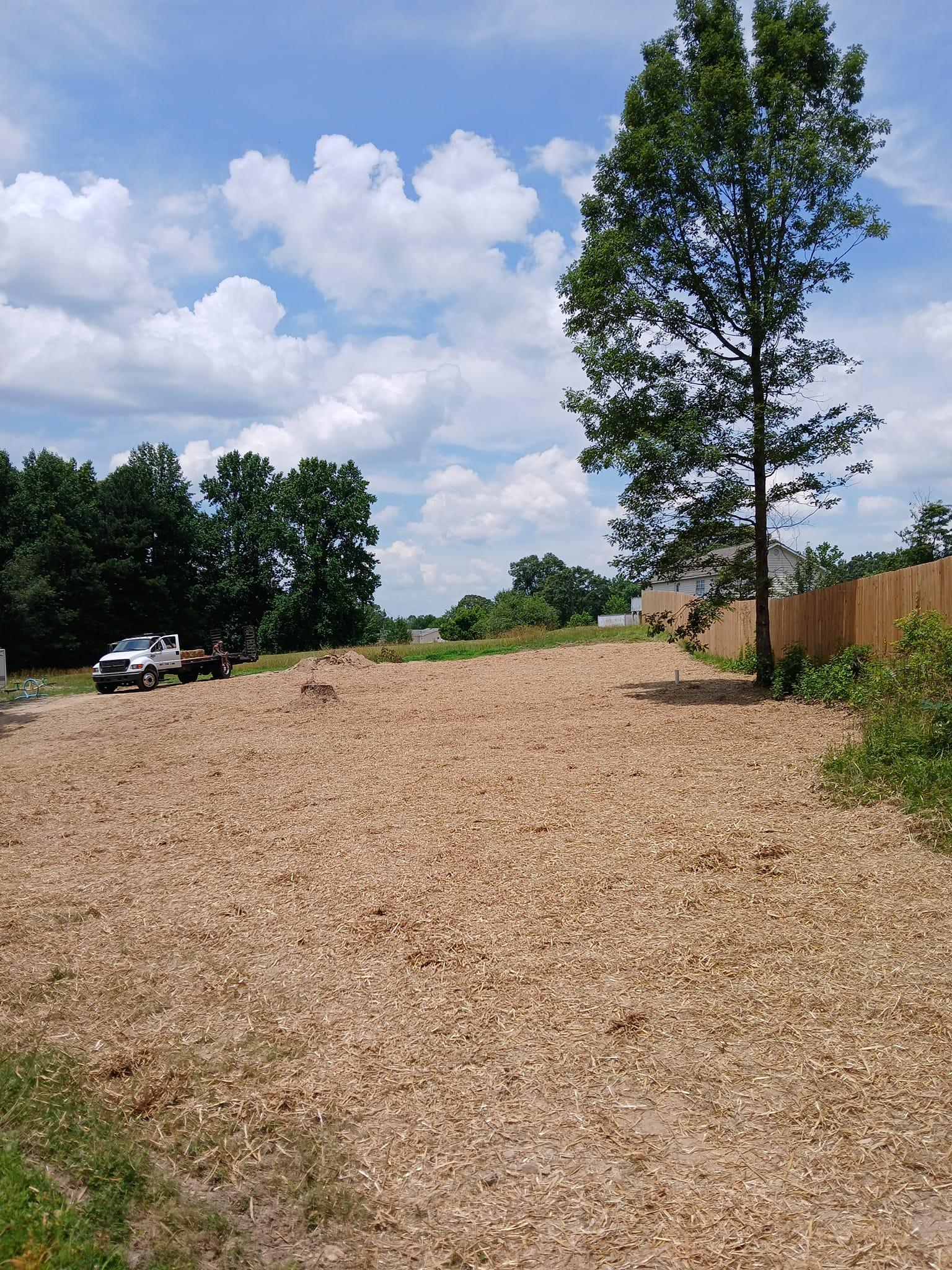 A large pile of wood chips in a field with trees in the background.