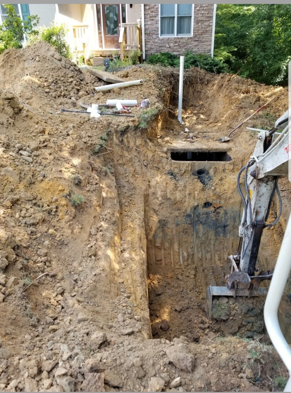 An excavator is digging a hole in the ground in front of a house.