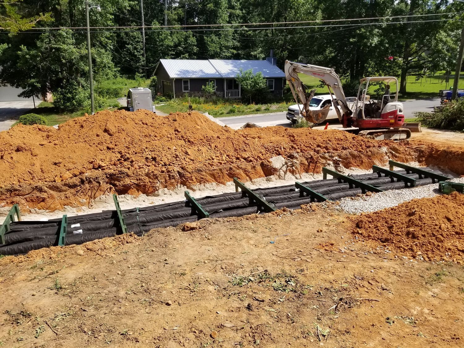 An excavator is digging a hole in the dirt in front of a house.