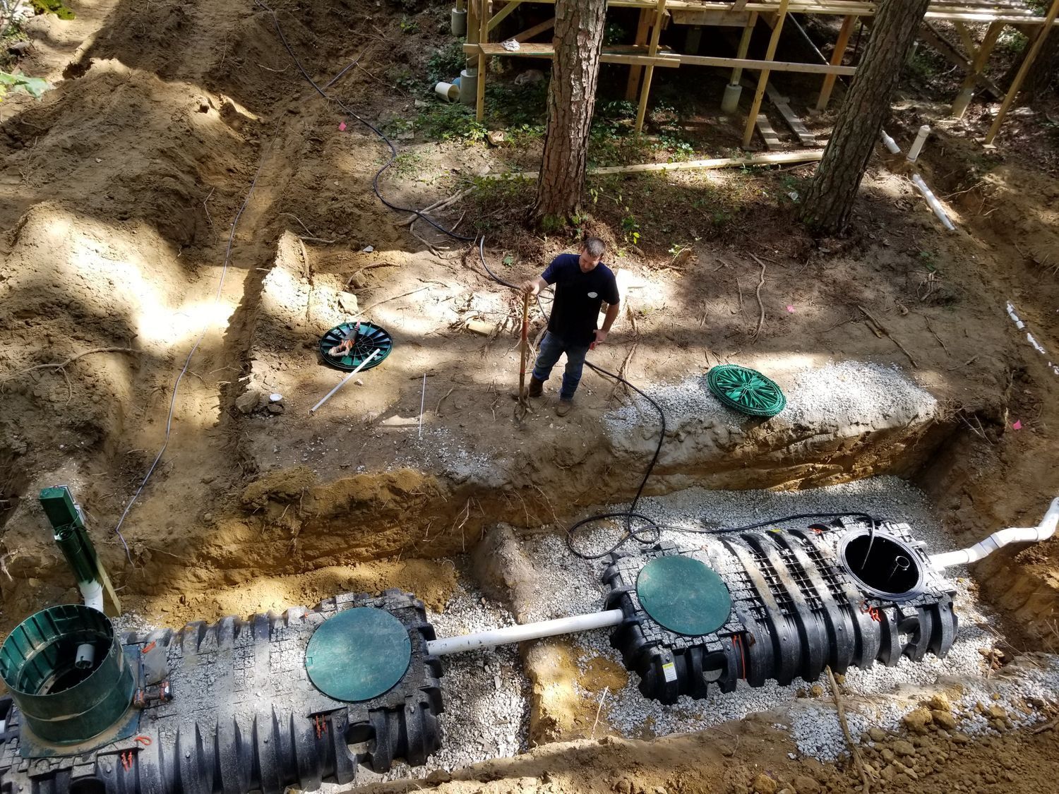 A man is standing in the dirt next to a septic tank.