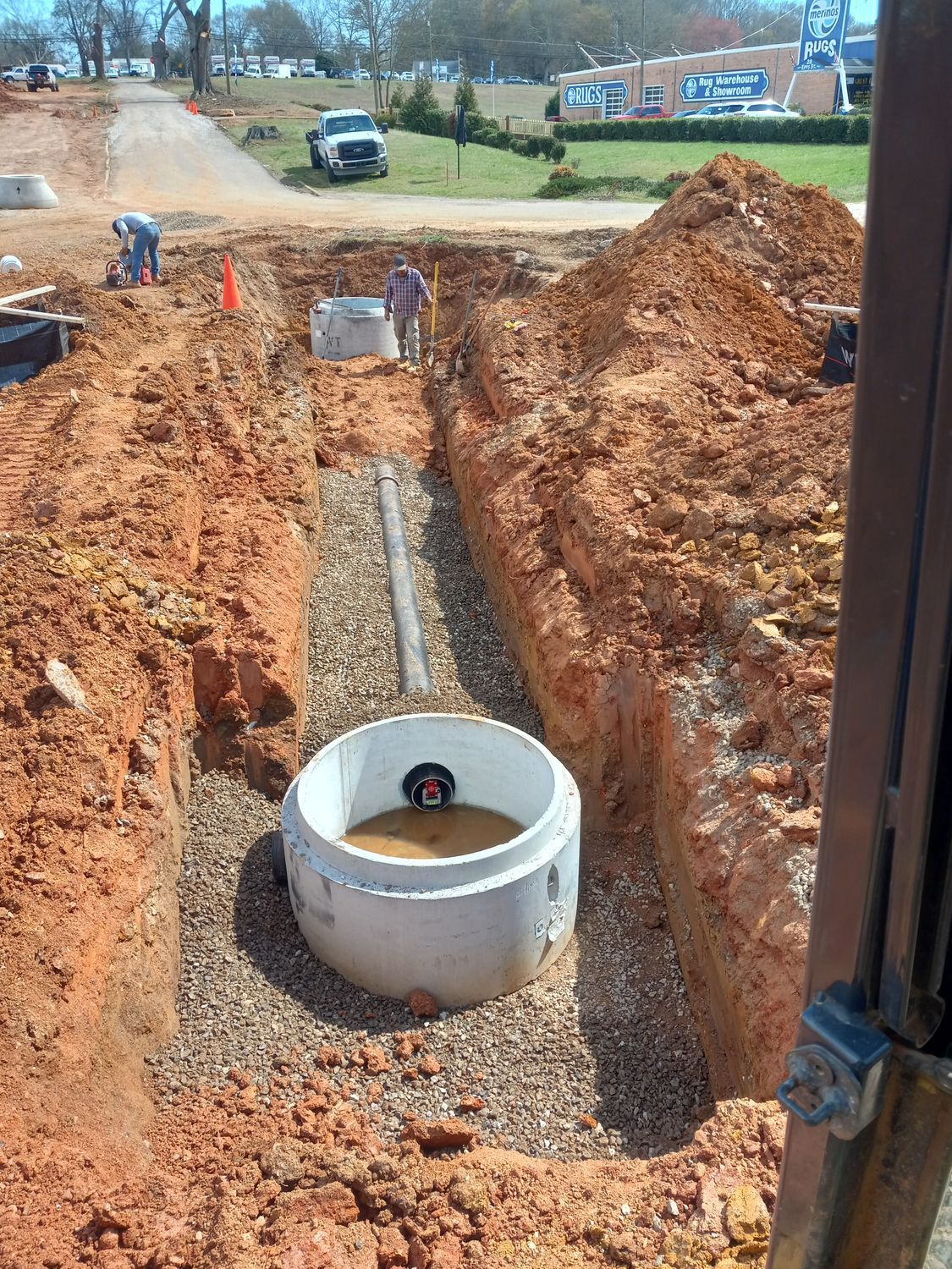 A manhole cover is being installed in a trench next to a road.