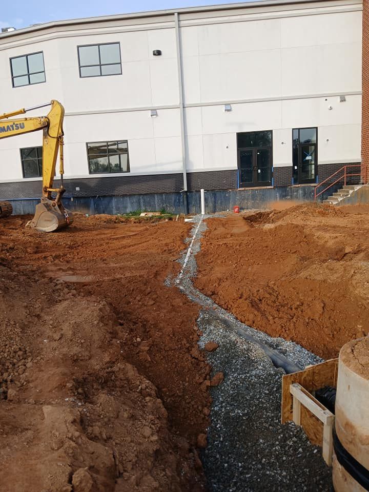 A yellow komatsu excavator is digging a trench in front of a building