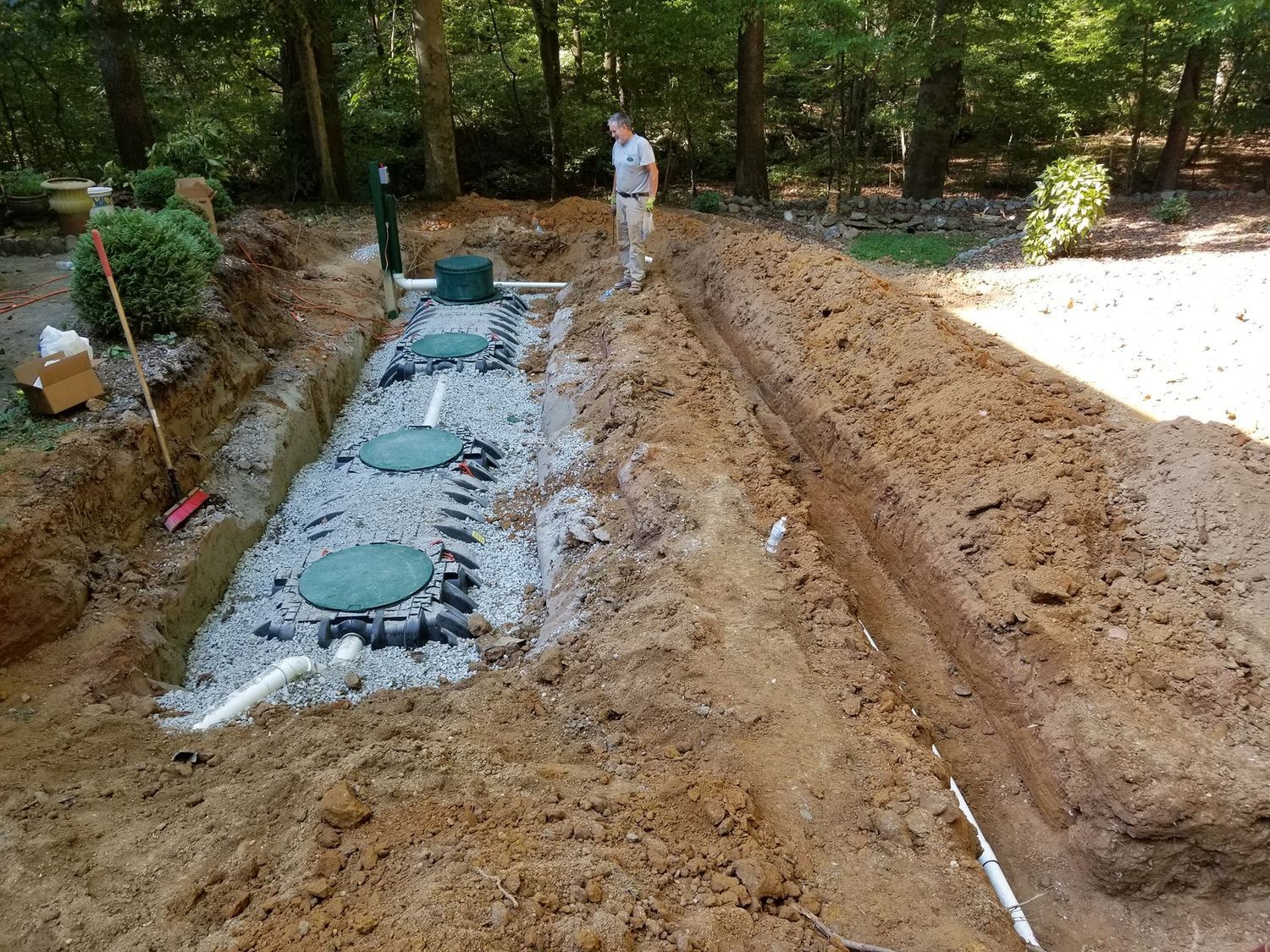 A man is standing in the dirt next to a septic tank.