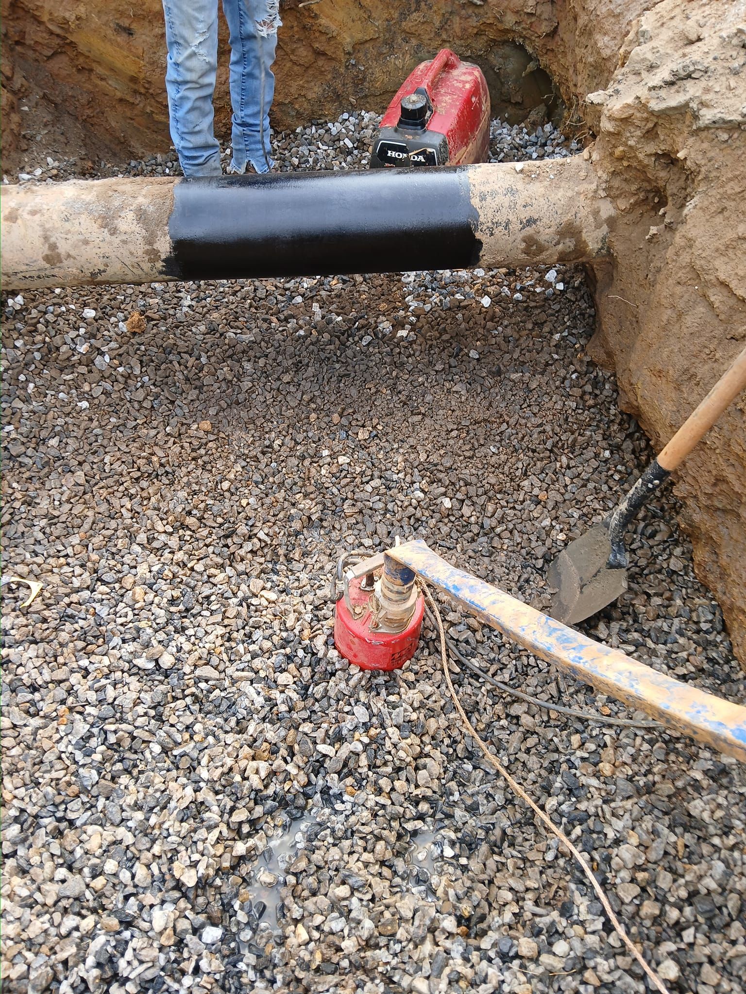 A person is standing next to a pipe in a hole.