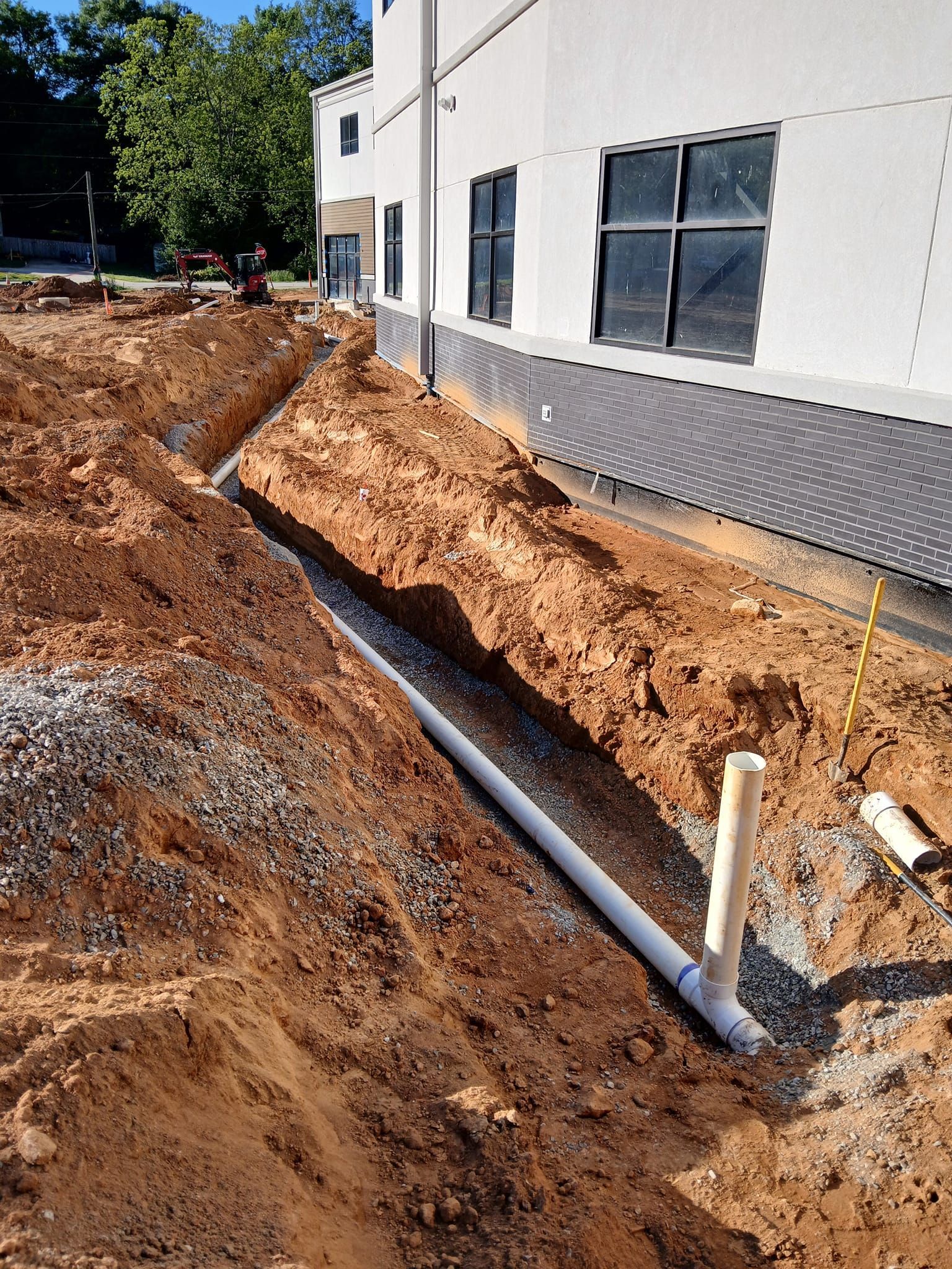A pipe is being installed in the dirt in front of a building.