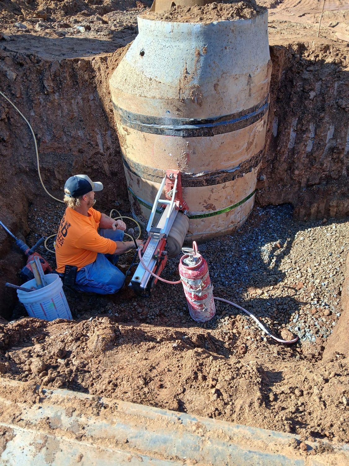 A man is kneeling in the dirt next to a large barrel.