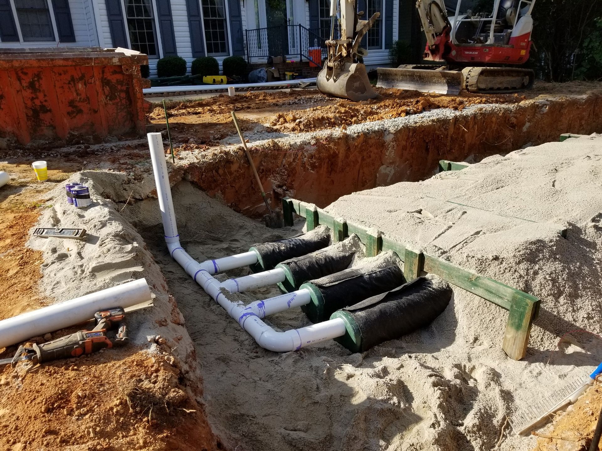 A drainage system is being installed in the dirt in front of a house.