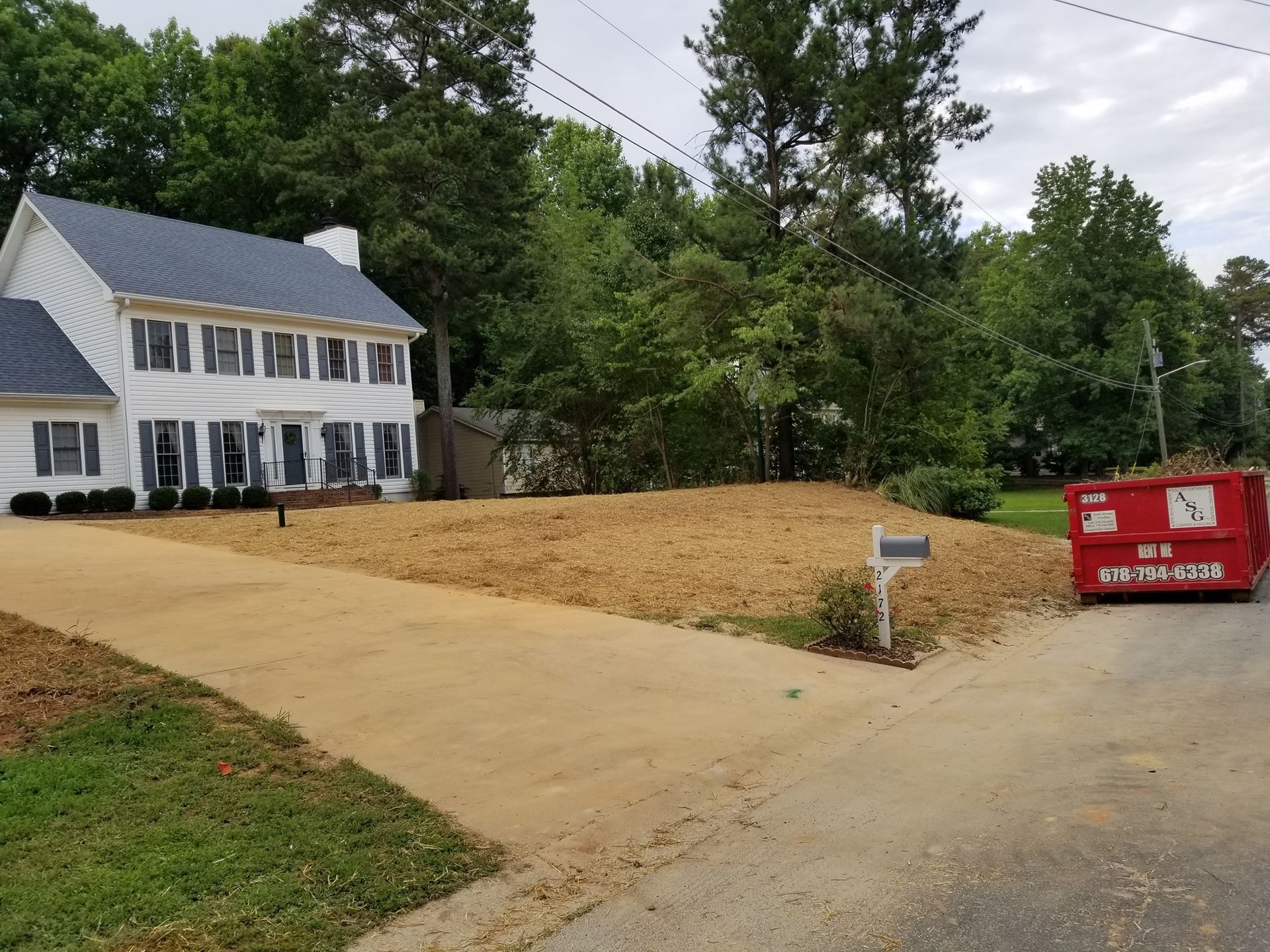 A large white house with a red dumpster in front of it.
