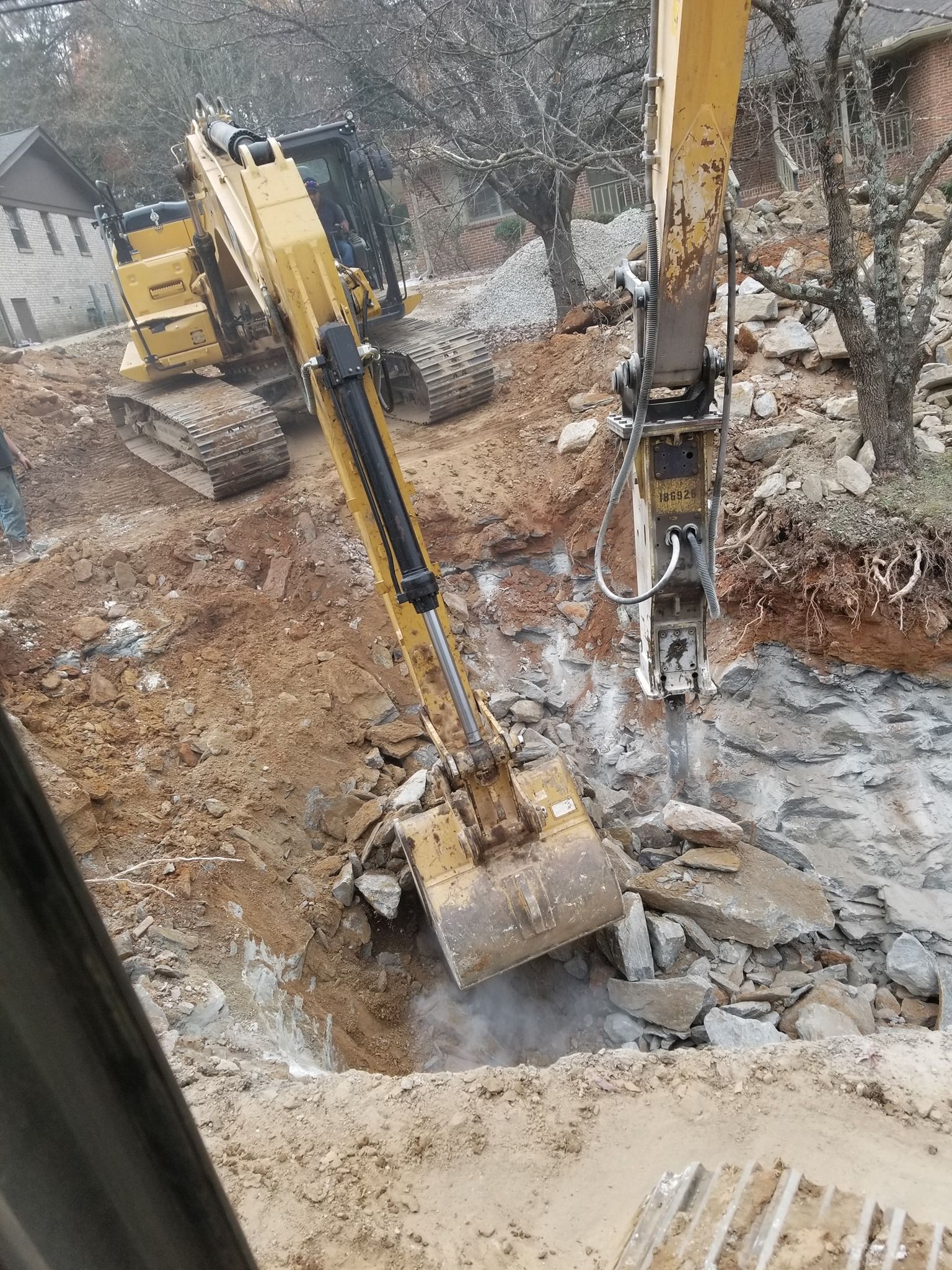 A yellow excavator is breaking concrete on a construction site.