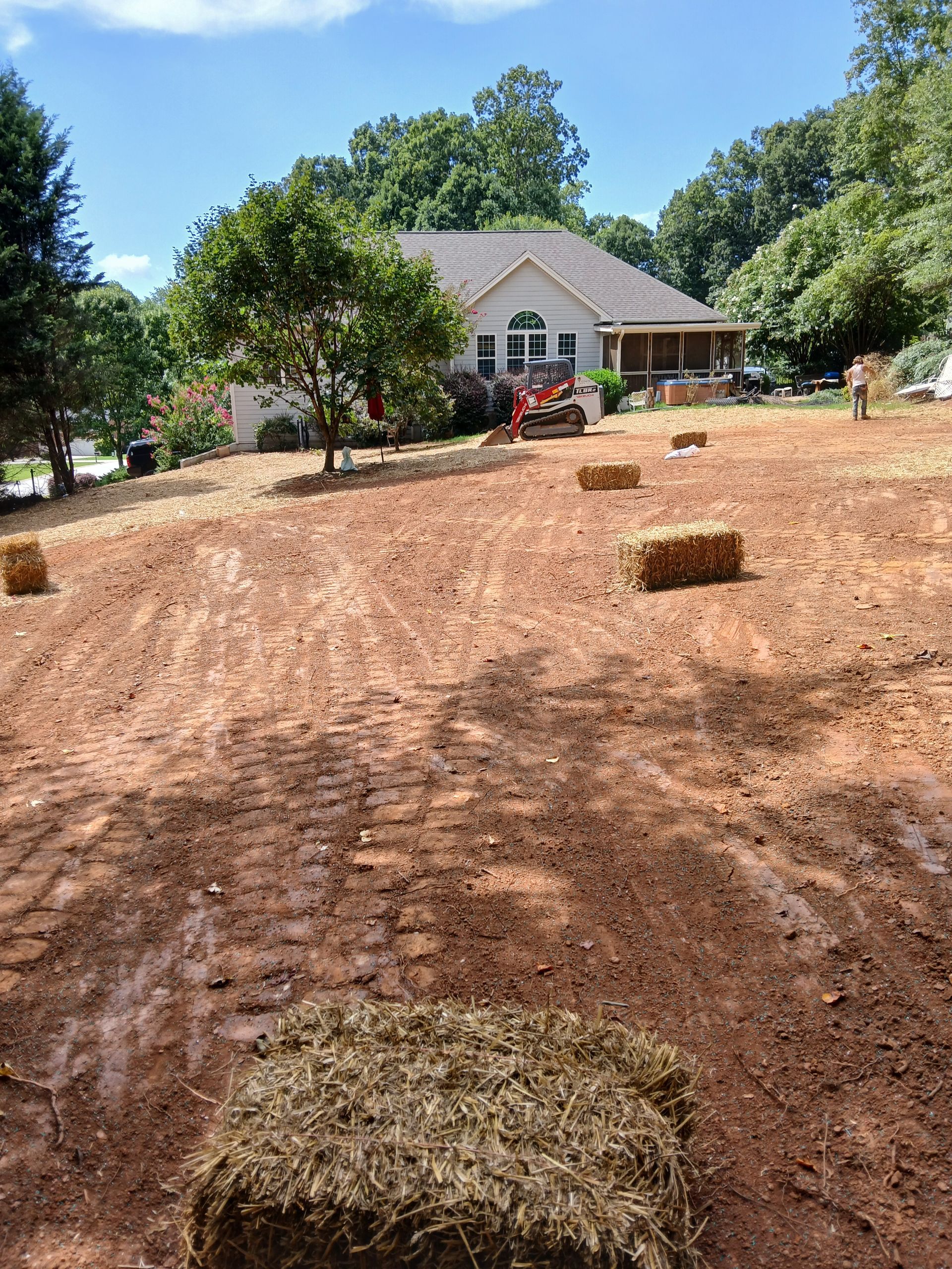 A pile of hay bales in a dirt field in front of a house.