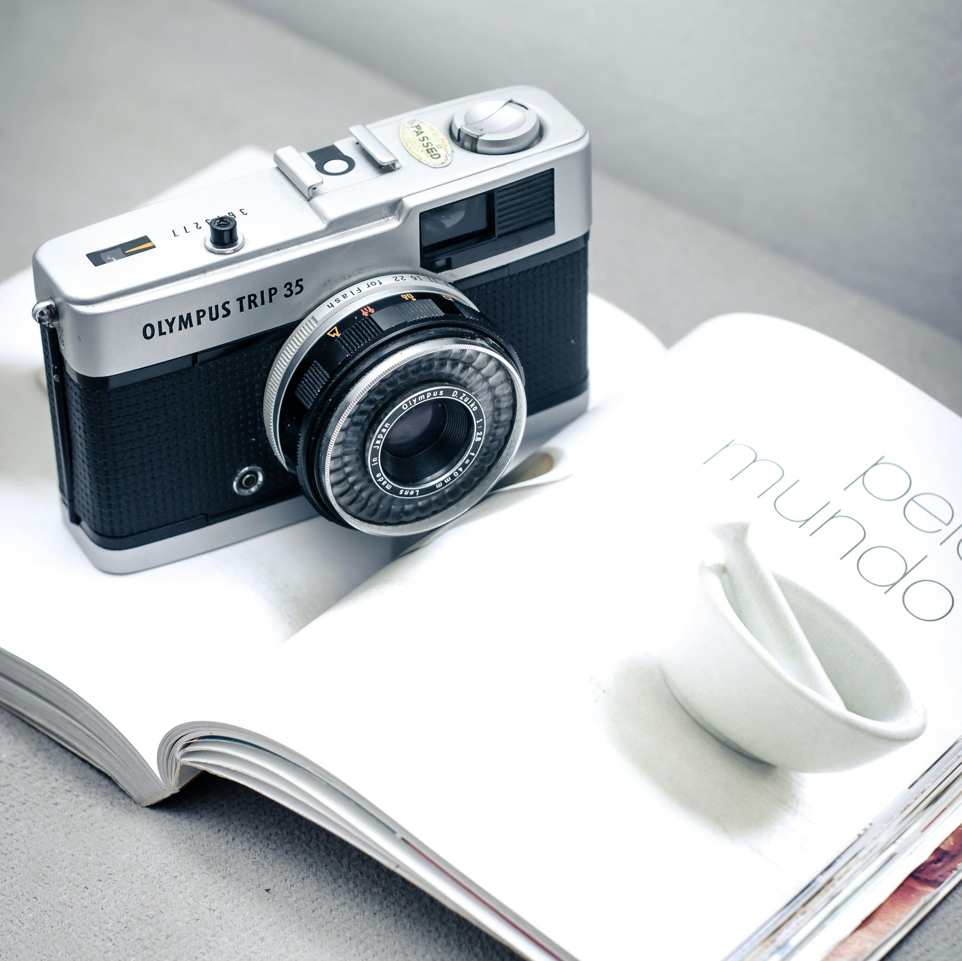 מצלמת אולימפוס טריפ 35 על ספר פתוח עם קערה לבנה קטנה.