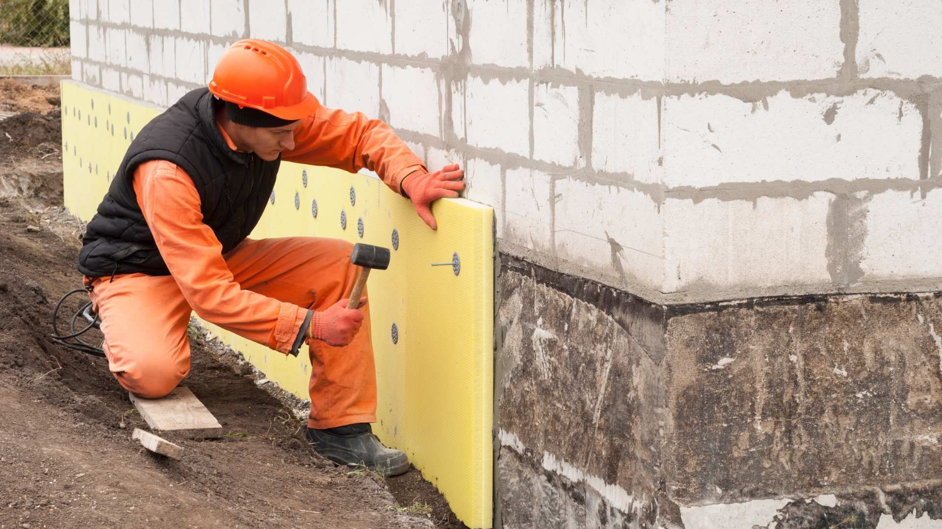 A man is hammering a piece of styrofoam on a wall.