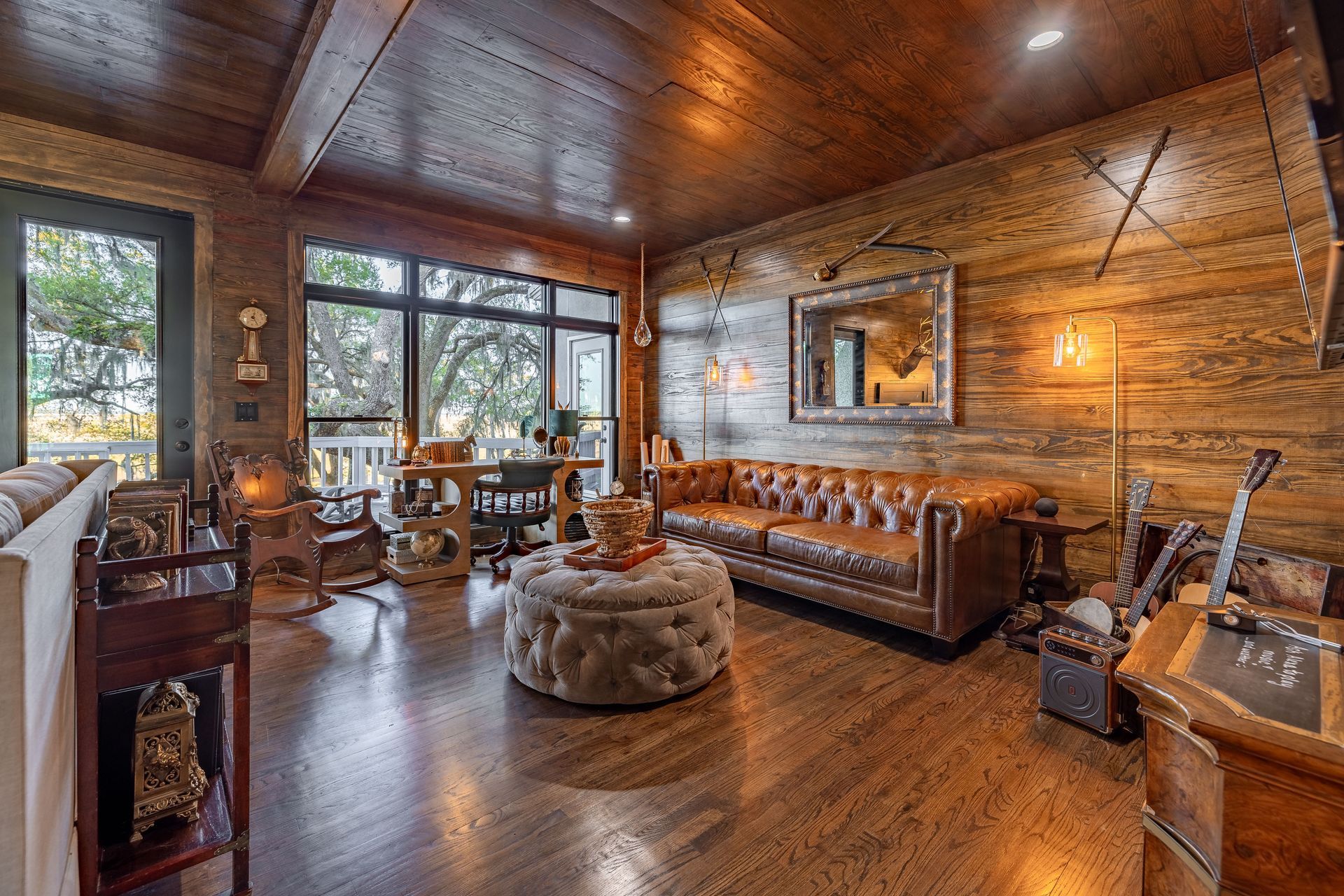 Rustic living room with wood paneling, leather sofa, and large windows.