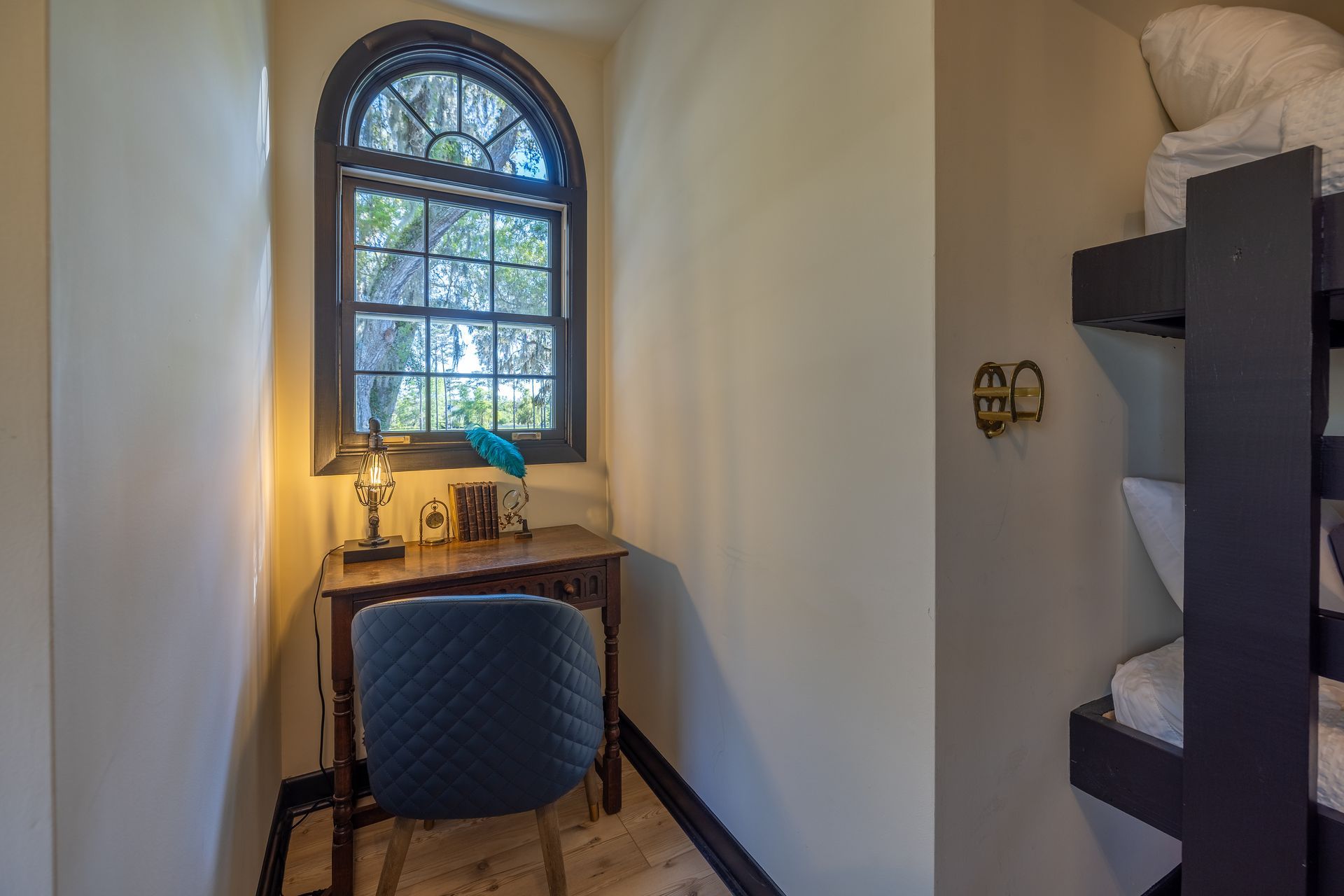 Small desk by arched window; bunk beds to the right. The room is tan with a black trim.