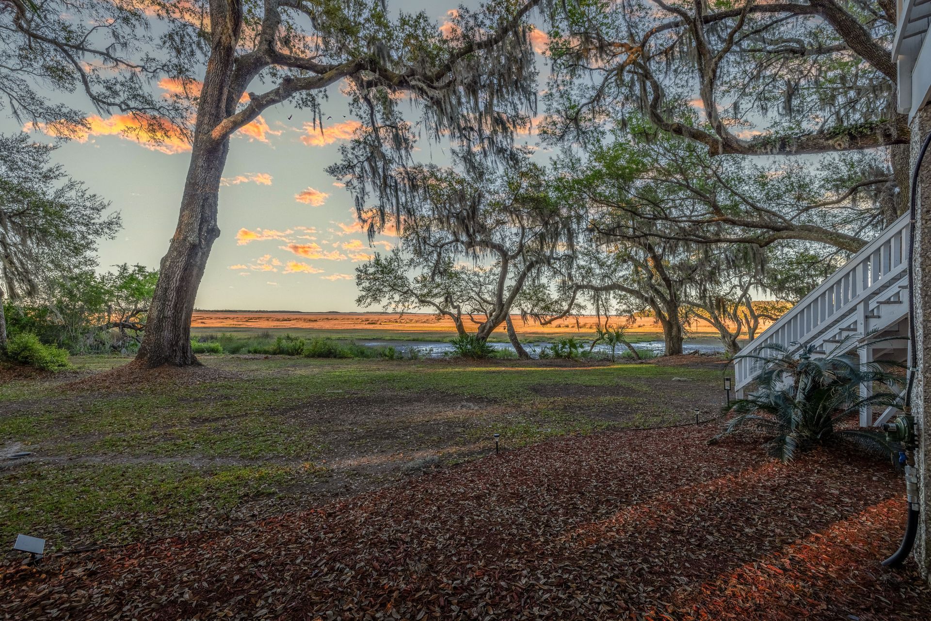 A sunset over a body of water with trees in the foreground and a house in the background.