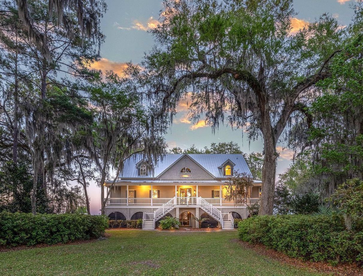 A large white house with a blue roof is surrounded by trees and flowers.