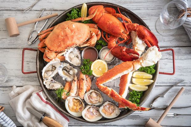 A pan filled with crabs , lobsters , oysters , and shrimp on a wooden table.