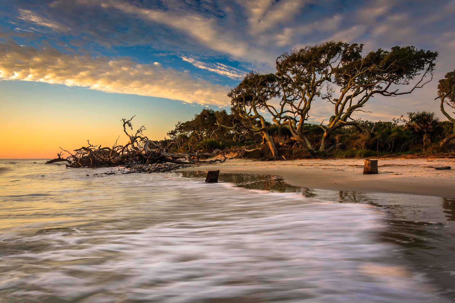 A long exposure photo of a beach at sunset with trees in the foreground.