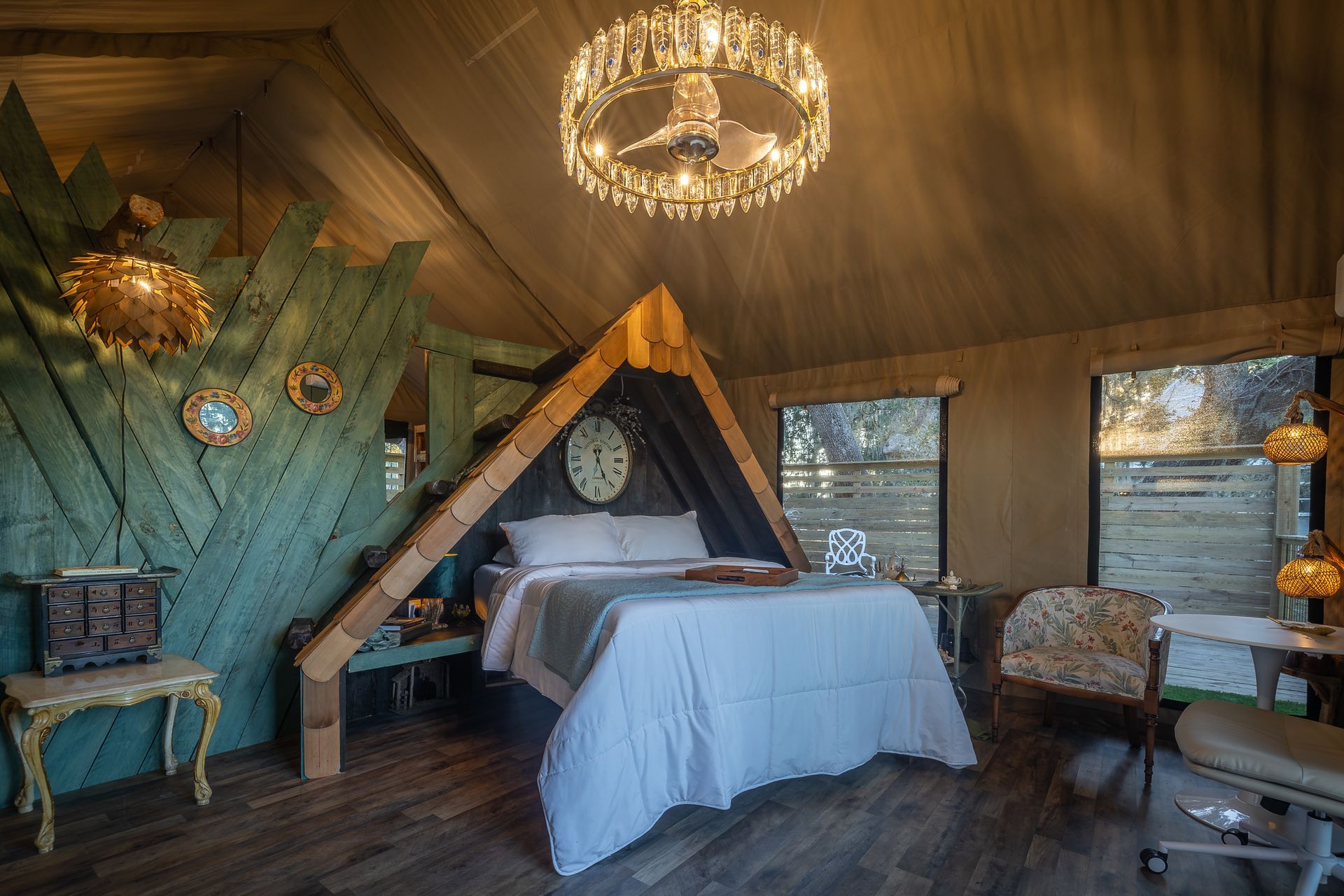 Cozy glamping tent interior with bed, chandelier, and a decorative wooden headboard.